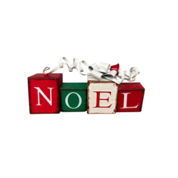 Red and green wooden blocks spelling "NOEL" with holiday decorations, standing on a mantel with a mirror and Christmas tree in the background.