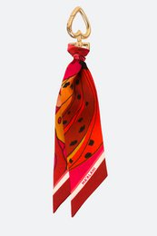 Vibrant red and orange scarf keychain with a heart-shaped metal charm. Stylish accessory featuring a bold, patterned fabric in a long, flowing design.