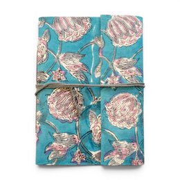 Notebook covered with violet printed fabric featuring floral patterns and designs.
The notebook is covered in a violet-colored printed fabric with a floral pattern. The design includes stylized flowers and leaves in shades of purple, blue, and pink. The fabric has a textured, embroidered-like appearance, adding visual interest to the notebook cover.