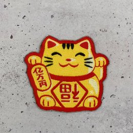 A colorful, embroidered patch depicting a traditional Japanese lucky cat or Maneki Neko. The patch features a smiling cat with raised paw, a common symbol of good fortune and prosperity.