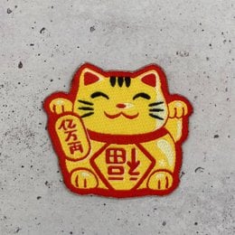 A colorful, embroidered patch depicting a traditional Japanese lucky cat or Maneki Neko. The patch features a smiling cat with raised paw, a common symbol of good fortune and prosperity.