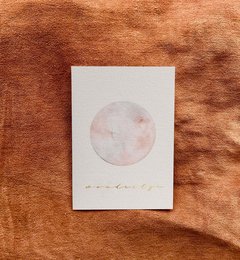 A pastel-colored illustration of a full moon on a white card against a warm, textured background.