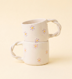 White ceramic mug with braided rope handle, colorful floral daisy pattern, modern minimalist design.