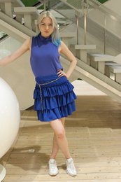  A blue ruffled skirt with a high-neck sleeveless top. The skirt has multiple tiers of ruffles in a vibrant blue color. The model is wearing white sneakers.