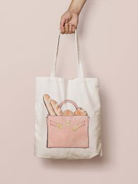 A white tote bag with a pink leather handbag illustration and the text 'Baguette' printed on it. The bag is being held by a person's hand.