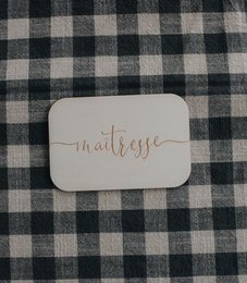 Wooden greeting cards with the text "Maîtresse, Maître, Nounou" (Mistress, Master, Nanny) in cursive font. The cards are displayed on a black and white checkered fabric background.
