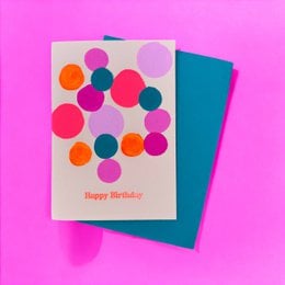 A colorful birthday card with a pattern of vibrant circles in various shades of pink, orange, and blue against a light beige background. The text "Happy Birthday" is printed on the card.