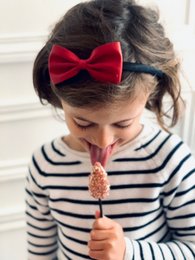 A red bow tie headband worn by a young girl with dark hair and a striped shirt.