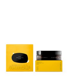 A gold-colored regenerating balm in a glass jar with a black label. The product is designed for skincare and claims to have regenerative properties.