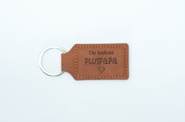Leather keychain with the text "The nicest pluspapa" engraved on it. Rectangular shape with a metal ring for attaching to keys.