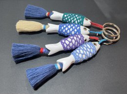 Colorful, striped fish-shaped keychains made of wood and wrapped in yarn.